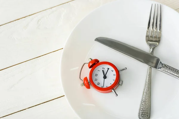 Top view of white plate with cutlery near red alarm clock on wooden surface — Stock Photo