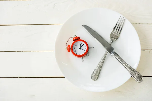 Top view of white plate with cutlery and red alarm clock on wooden surface — Stock Photo