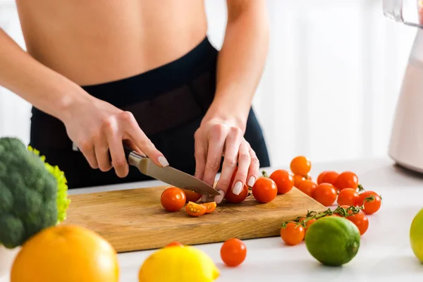 Cropped view of woman cutting cherry tomatoes on wooden cutting board — Stock Photo