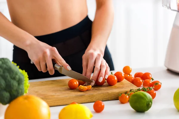 Abgeschnittene Ansicht einer Frau, die Kirschtomaten auf einem Holzschneidebrett schneidet — Stockfoto