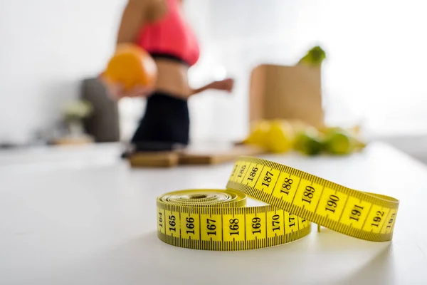 Selective focus of yellow measuring tape near woman holding orange in kitchen — Stock Photo