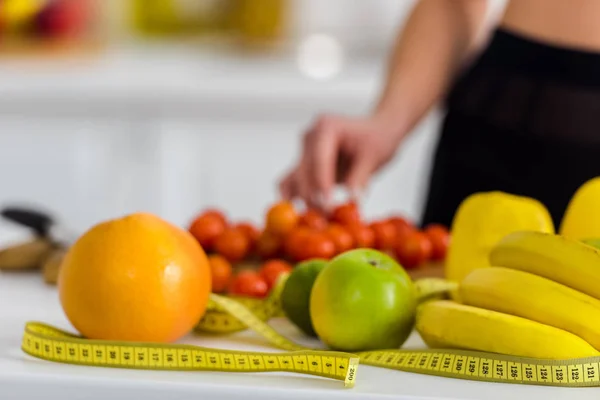 Vista cortada de mulher tomando tomate cereja perto de fita métrica na cozinha — Fotografia de Stock