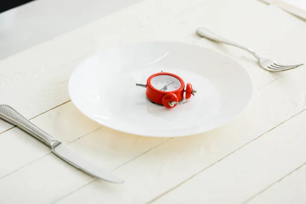 White plate with cutlery near red alarm clock on wooden surface — Stock Photo