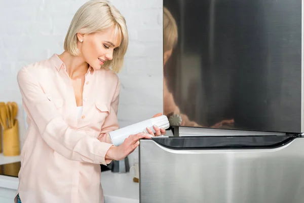 Cheerful blonde pregnant woman looking at can with whipped cream near — Stock Photo