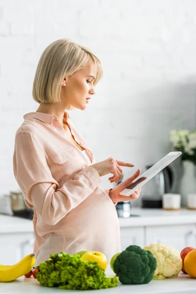 Привлекательная беременная женщина с помощью цифрового планшета на кухне — стоковое фото