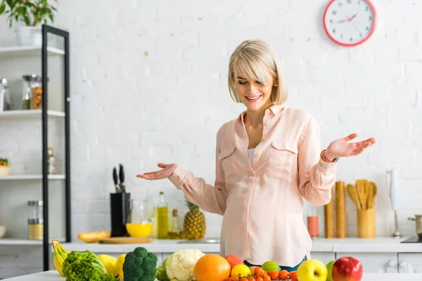 Cheerful blonde pregnant woman gesturing near fruits and vegetables — Stock Photo