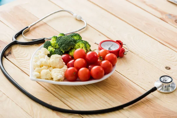 Organic vegetables on plate near stethoscope on wooden surface — Stock Photo