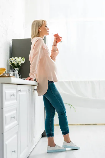 Beautiful blonde pregnant woman drinking smoothie in kitchen — Stock Photo