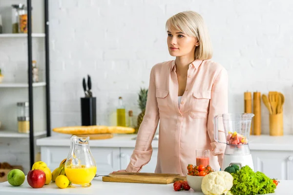Привлекательная беременная блондинка, стоящая рядом с овощами и фруктами на кухне — стоковое фото