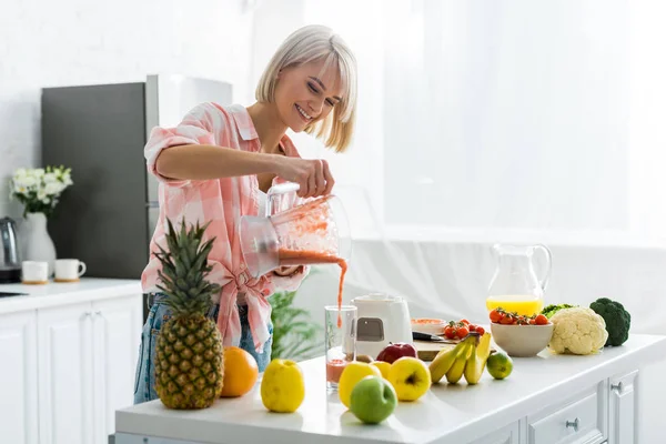 Joyeuse jeune femme versant savoureux smoothie en verre — Photo de stock