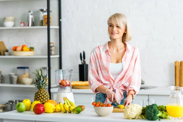 Junge Frau schneidet Kiwi-Früchte in der Nähe von Zutaten in Küche — Stockfoto