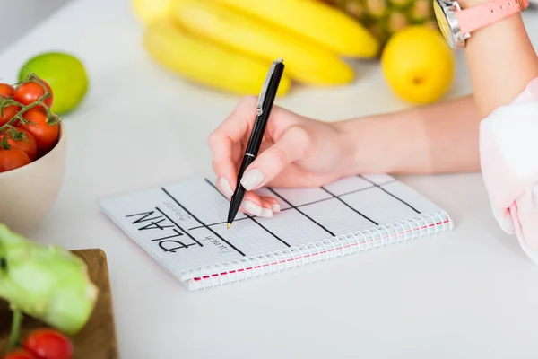 Cropped view of woman writing in notebook with plan lettering near ingredients — Stock Photo