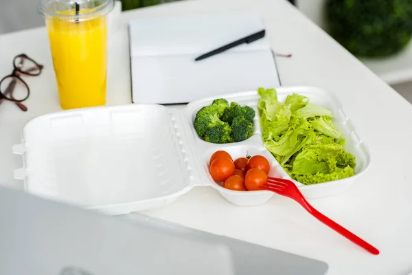 Tasty organic vegetables near plastic fork and notebook with pen — Stock Photo