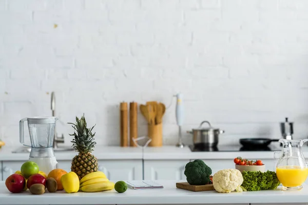 Органические вкусные фрукты и овощи рядом блендер и кувшин с апельсиновым соком — стоковое фото