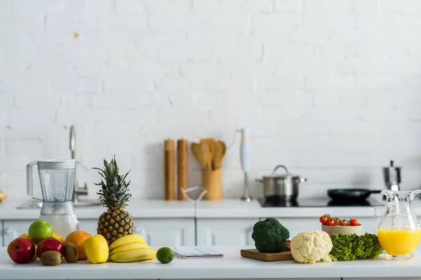 Organic tasty fruits and vegetables near blender and jug with orange juice — Stock Photo