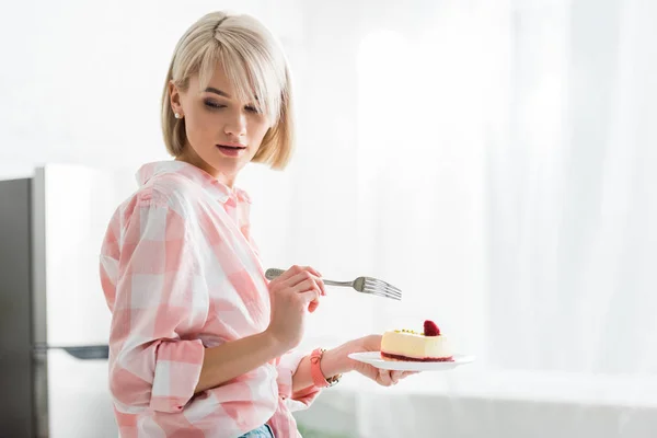 Chica rubia sosteniendo tenedor y platillo con pastel dulce - foto de stock