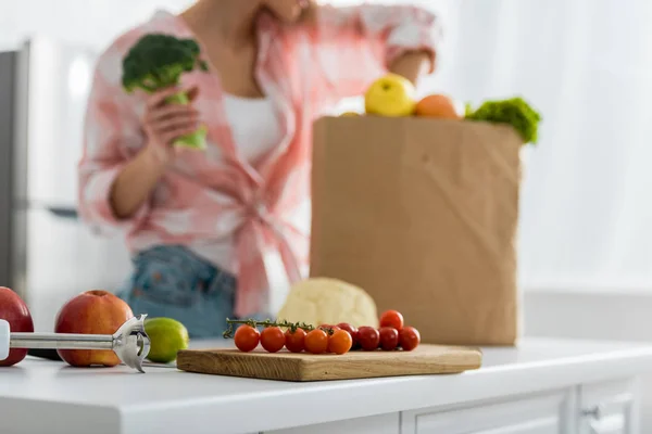 Foco seletivo de tábua de corte com tomates cereja vermelhos perto da mulher — Fotografia de Stock