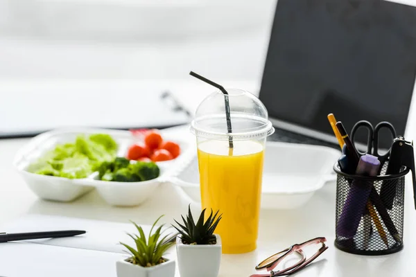 Zumo de naranja y plantas verdes cerca de verduras sabrosas y portátil con pantalla en blanco - foto de stock