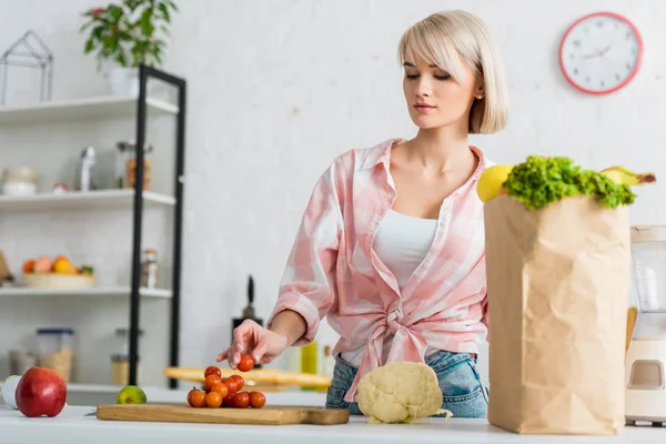 Attraktive blonde Frau schneidet Kirschtomaten auf Schneidebrett — Stockfoto