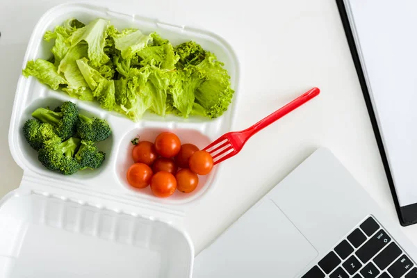 Top view of take away box with tasty vegetables near laptop — Stock Photo