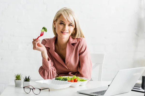 Fröhlicher Freiberufler hält Gabel mit Kirschtomate neben Laptop — Stockfoto