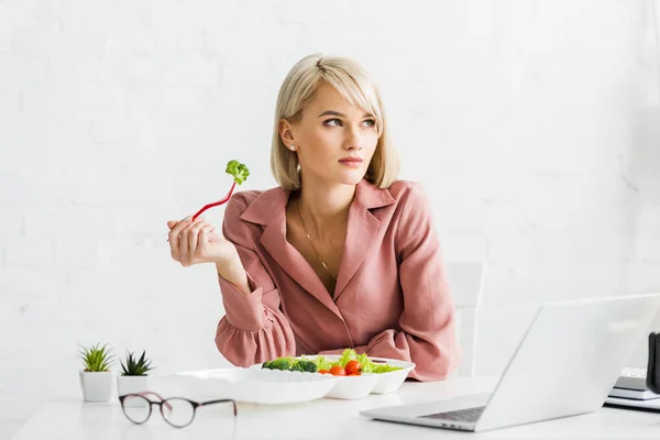 Freelancer atraente segurando garfo com brócolis perto do laptop — Fotografia de Stock