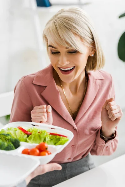 Vue recadrée de l'homme tenant boîte à emporter avec des légumes près excité femme blonde — Photo de stock