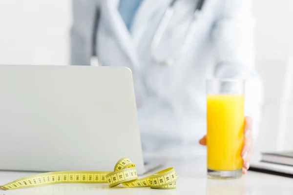 Cropped view of nutritionist holding glass of fresh orange juice near measuring tape — Stock Photo