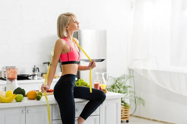 Attraente donna bionda in abbigliamento sportivo tenuta metro nastro vicino ingredienti in cucina — Foto stock