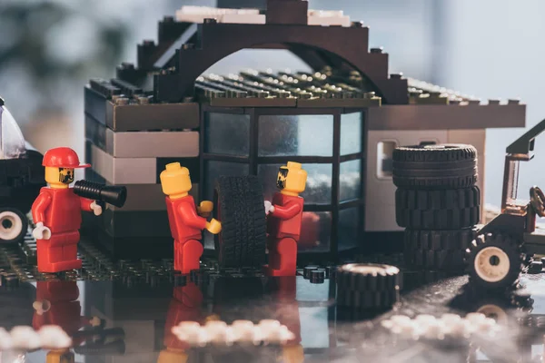 KYIV, UKRAINE - MARCH 15, 2019: lego minifigures in red carrying tire while other figurine shouting in mouthpiece at service station — Stock Photo