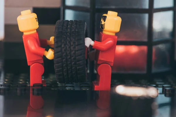 QUIIV, UCRÂNIA - MARÇO 15, 2019: close up of lego minifigures in red carrying tire on surface made of lego blocks — Fotografia de Stock