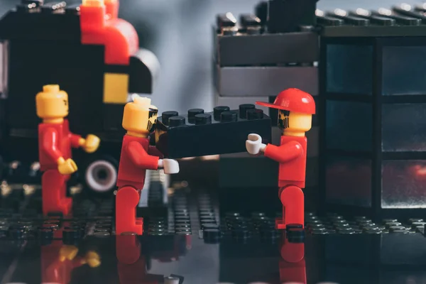 KYIV, UCRANIA - 15 de marzo de 2019: figuras de lego worker en rojo llevando bloque de lego negro - foto de stock