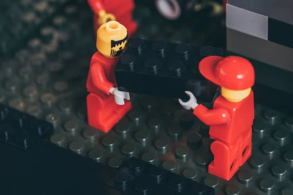 QUIIV, UCRÂNIA - MARÇO 15, 2019: close up of lego worker figurines in red carry black lego block — Fotografia de Stock