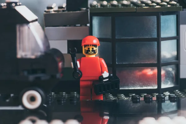 Kyiv, Ukraine - 15. März 2019: rote Lego-Arbeiterfigur mit Hut, Schraubenschlüssel und Werkzeugkiste in der Nähe eines Gebäudes aus Legosteinen — Stockfoto