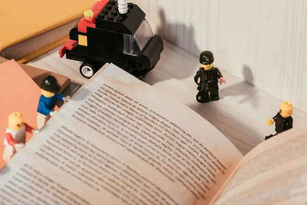 KYIV, UCRANIA - 15 de marzo de 2019: coloridas minifiguras de lego de plástico volteando la página del libro cerca de un camión de juguete - foto de stock