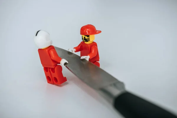KYIV, UCRANIA - 15 DE MARZO DE 2019: Figuras lego rojas portando cuchillo de metal sobre blanco - foto de stock