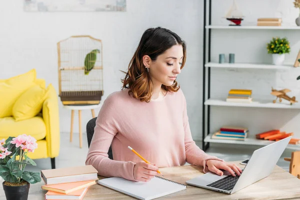 Schöne aufmerksame Frau, die zu Hause arbeitet, während sie zu Hause mit Laptop sitzt — Stockfoto