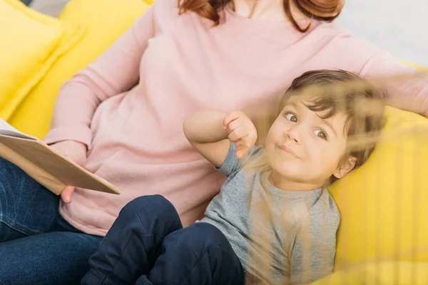 Partial view of woman with book sitting on sofa near adorable son — Stock Photo