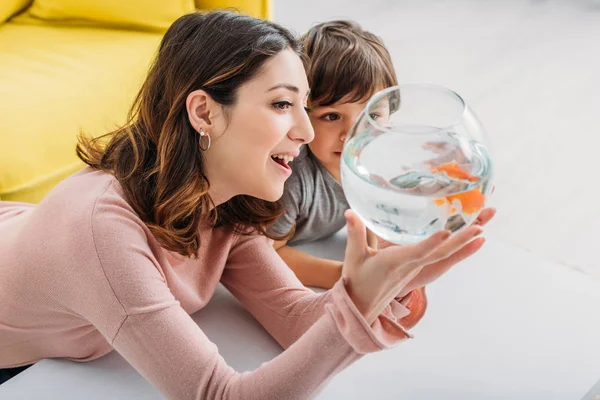 Sorrindo mulher atraente mostrando tigela de peixe para filho adorável — Fotografia de Stock