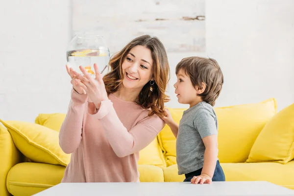 Bella madre allegra mostrando ciotola di pesce al figlio adorabile — Foto stock