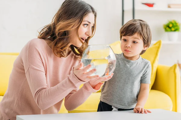 Hübsch lächelnde Mutter zeigt ihrem entzückenden Sohn Fischschale — Stockfoto