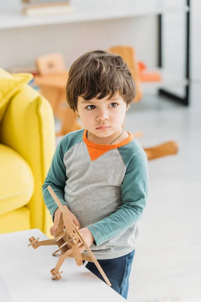 Прелестный серьезный ребенок держит деревянный самолет модель дома — стоковое фото