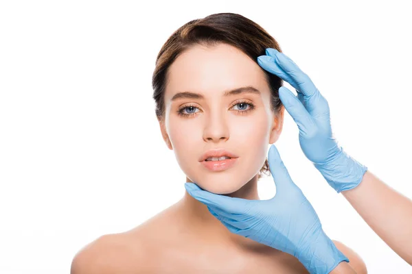 Обрезанный вид пластического хирурга в голубых латексных перчатках трогательное лицо красивой женщины изолированы на белом — стоковое фото