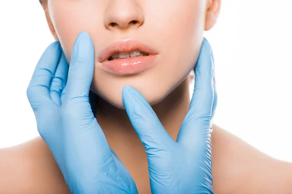 Vista recortada de cirujano plástico en guantes de látex azul tocando la cara de la mujer aislada en blanco - foto de stock