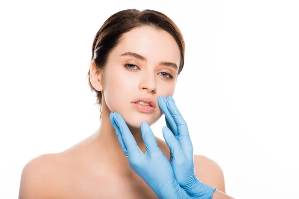 Обрезанный вид пластического хирурга в латексных перчатках трогательное лицо брюнетки женщина изолированы на белом — стоковое фото