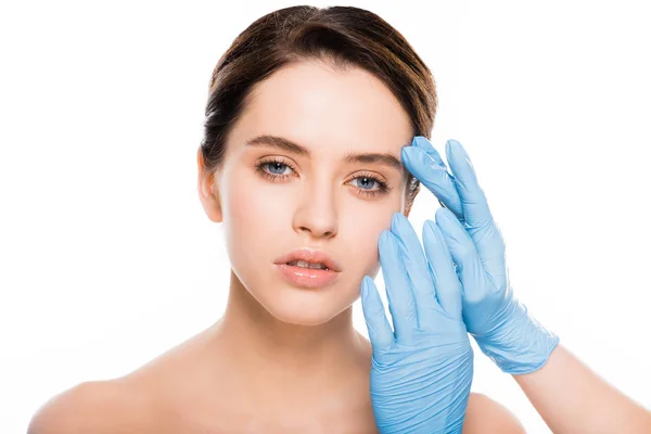 Visão recortada de cirurgião plástico em luvas de látex tocando rosto de mulher morena isolada em branco — Fotografia de Stock