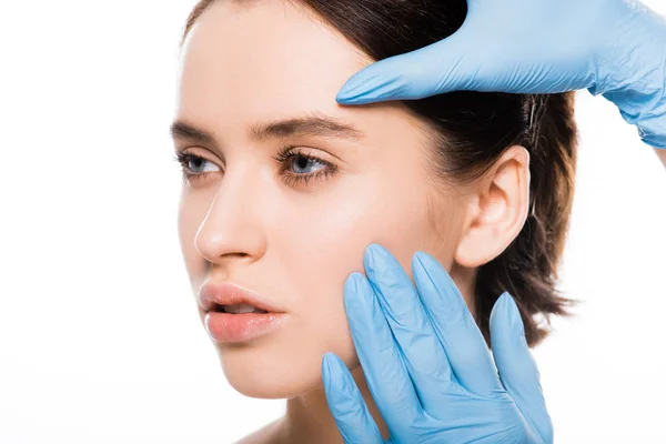 Primer plano de cirujano plástico en guantes de látex tocando la cara de mujer atractiva aislada en blanco - foto de stock