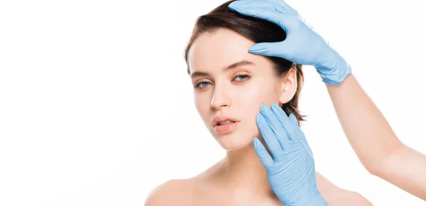 Colpo panoramico di chirurgo plastico in guanti di lattice volto toccante di donna attraente isolato su bianco — Foto stock