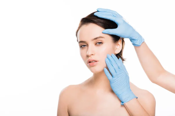 Vista recortada de cirujano plástico en guantes de látex tocando la cara de chica atractiva aislada en blanco - foto de stock