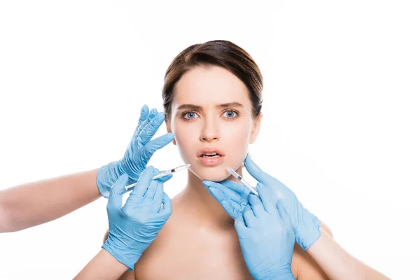 Abgeschnittene Ansicht von Kosmetikerinnen in Latexhandschuhen, die das Gesicht eines schockierten Mädchens berühren, während sie Spritzen isoliert auf weiß halten — Stockfoto